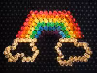 A colorful rainbow made from translucent pegs on a dark pegboard, with two hand shapes in yellow below it, creating a vibrant and creative design.