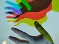A hand is placed on a screen, creating multiple colored shadow silhouettes in red, green, and blue. The effect results in a striking and colorful display reminiscent of Colorado art around the hand on the screen.