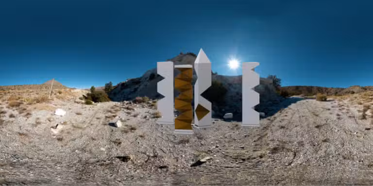 Futuristic sculptures with geometric designs and metallic finishes stand in a dry, rocky landscape, reminiscent of a Colorado Burning Man event. Under the clear blue sky, the sun shines brightly above, casting shadows on the ground.