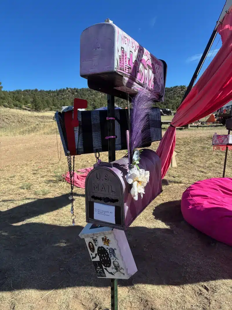 Decorated mailboxes stacked on a post beside pink drapes and a pink bean bag at the Love Letters installation.