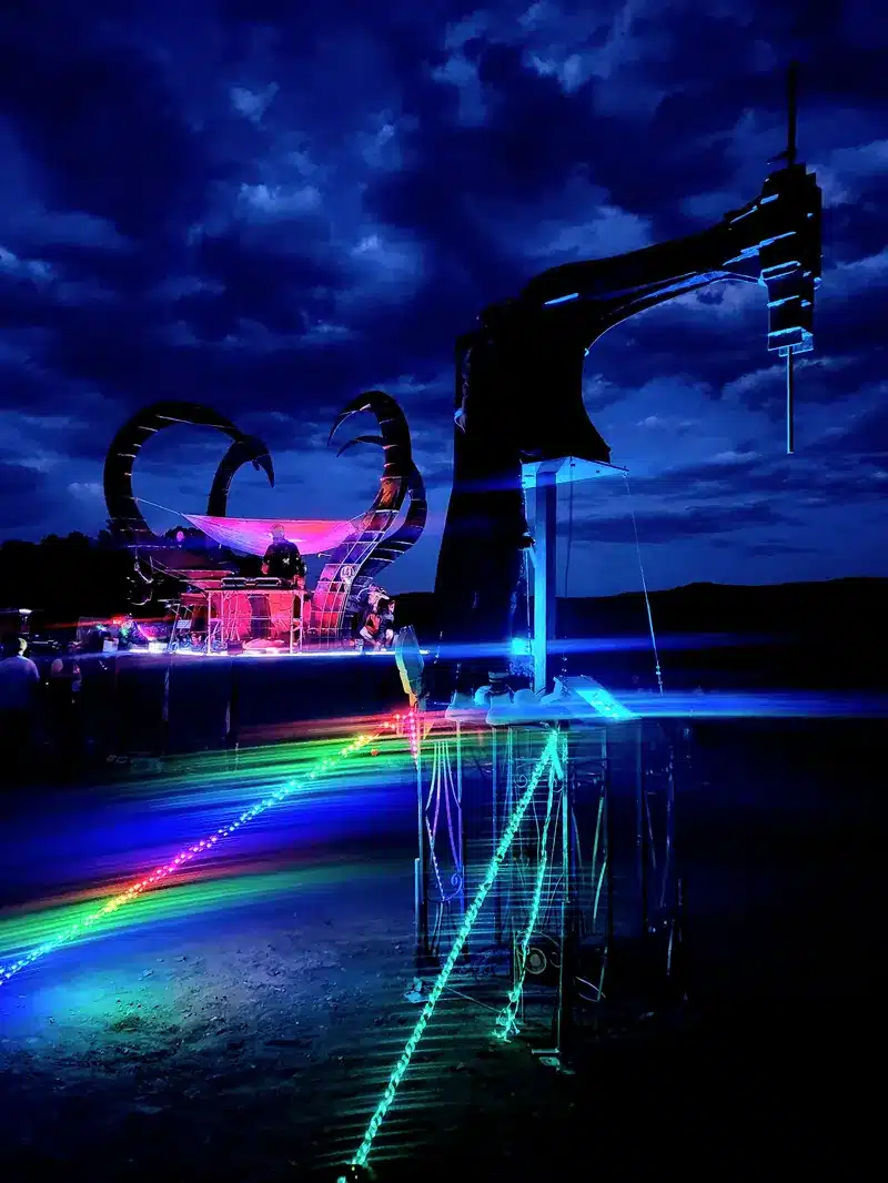 Organicus Mechanicus, a mechanical structure with curling horns, glowing with neon and laser light under a deep blue night sky.