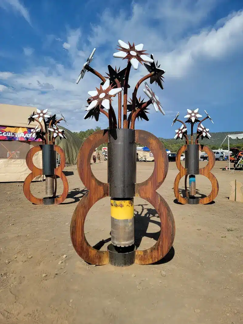 Three rusted-steel planters shaped like figure eights, each holding a bouquet of cut-metal flowers, under a bright sky.