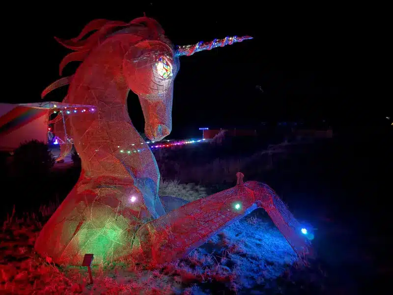 The giant wire-mesh unicorn sculpture lit red at night, with a stained-glass eye and a string of lights along its horn.